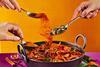 An image showing hands placing spices into a pan of curry