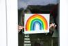 An image showing a woman placing a rainbow drawing on her window