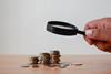 An image showing a magnifier being held on top of stacks of coins