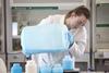 An image showing a woman pouring a blue liquid from a big plastic tank into smaller plastic containers