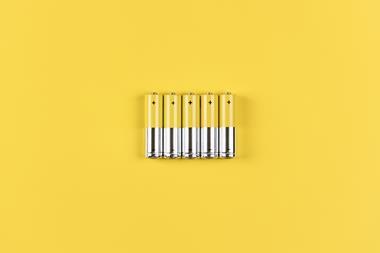 Photo of five grey-yellow alkaline AA batteries on a yellow background.