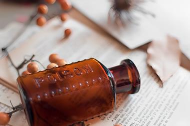 Image of a brown poison bottle lying on a book and notes, surrounded by poison pills