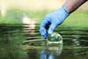 Close up of a gloved hand collecting a water sample with a beaker