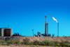 An oil drilling platform with a burning flare in a dry landscape under a clear blue sky