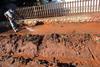 A man in protective clothing uses a jet wash to clean red mud from the pavement