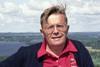 A headshot of Martti Harmoinen wearing a red shirt and black cardigan in the countryside