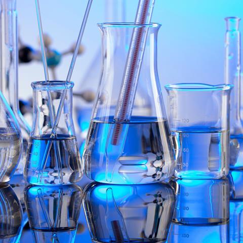 Various types of laboratory glassware, a thermometer and stirrers sitting on a surface with a blue background